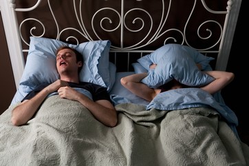 Young man snoring, woman covering face with pillow